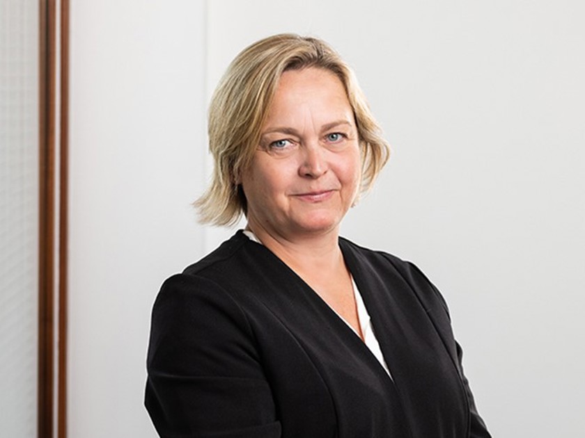 A woman wearing a black shirt and a black jacket, standing confidently with a neutral expression.