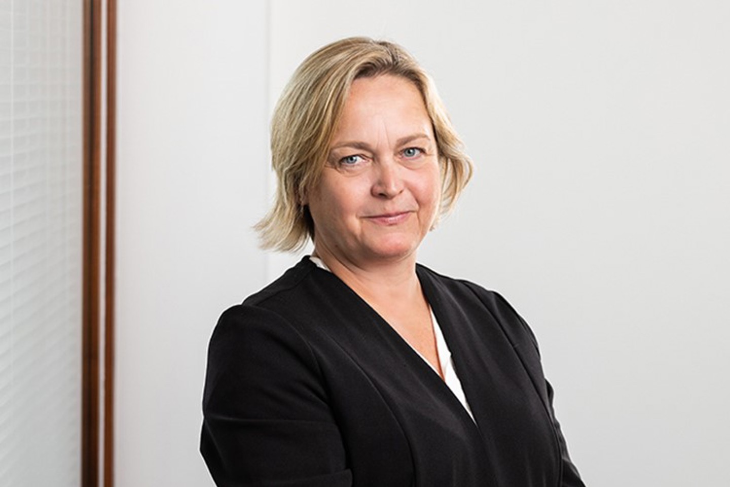 A woman wearing a black shirt and a black jacket, standing confidently with a neutral expression.